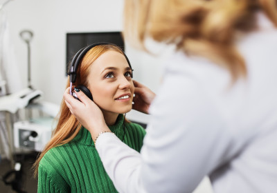 A young lady with red hair gets her hearing tested by an audiologist