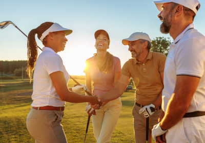 A group of multicultural friends shake hands during a game of golf near sunset